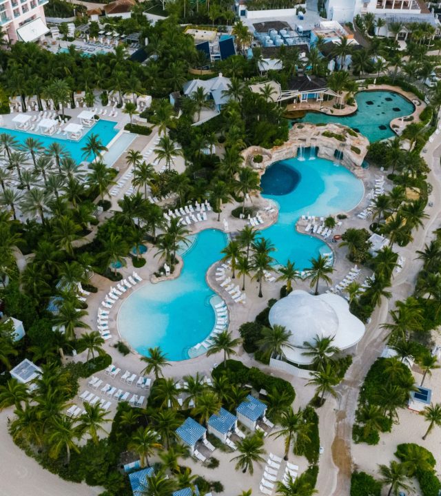 A stunning aerial view of a luxurious beachfront resort with swimming pools and palm trees.